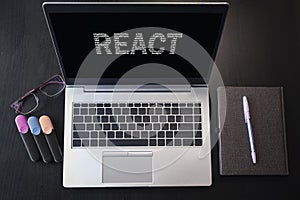 Top view of laptop with text React. React inscription on laptop screen and keyboard. Learn react language, computer courses,