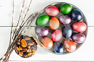 Top view of a large plate with Easter multi-colored eggs and willow twigs. white wooden background
