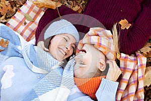 Top view of laughing family of young woman, teenage girl hugging, lying head-to-head on yellow fallen leaves in forest.