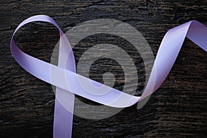 Top view of lavender or light purple orchid color ribbon on dark wooden background. General and testicular cancer and epilepsy.