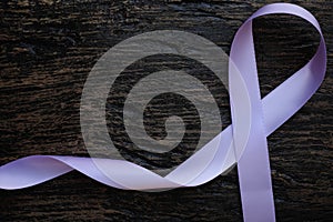Top view of lavender or light purple orchid color ribbon on dark wooden background. General and testicular cancer and epilepsy.