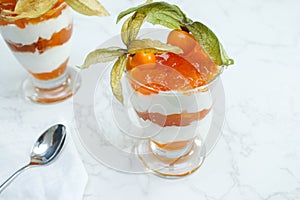 Top view of layered dessert with protein yoghurt and physalis fruit in a glass jar, on marble table