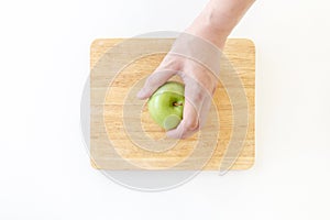 Top view of Left hand grab a green apple in wooden chopping board on white background