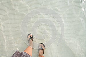 Top view legs in black flip flop underwater of sea on the beach with white wave sand. vacation summer in a holiday