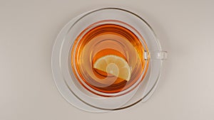 TOP VIEW: Lemon slice swims in a black tea in a glass tea cup with a dish