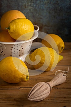 Top view of lemons in drainer on rustic table with wooden squeezer,
