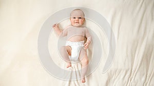 Top view of little baby boy in diapers lying on soft white blanket on bed.