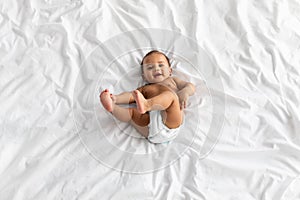 Top view of little black baby lying on bed at home
