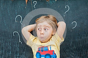 Top view of a little blond kid boy with question mark on blackboard. Concept for confusion, brainstorming and choice