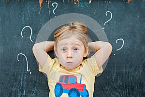 Top view of a little blond kid boy with question mark on blackboard. Concept for confusion, brainstorming and choice