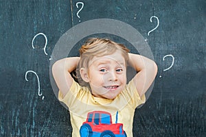 Top view of a little blond kid boy with question mark on blackboard. Concept for confusion, brainstorming and choice