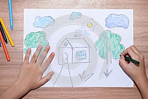 Top view of a little boy drawing a house with crayons is a beautiful imagination painting. A child`s hand is engaged in creativit