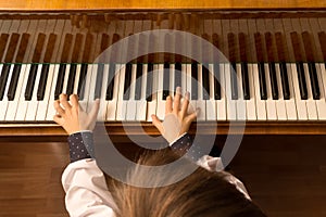 Top view of a little boy playing the piano. Head and hands in white shirt in the frame. Selective focus on fingers and