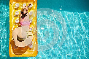 Top view little girl in hat relaxing in swimming pool, swims on inflatable yellow mattress
