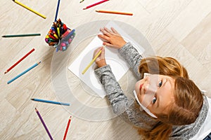 Top view of little girl painting, looking at camera and sitting on the floor in her room at home