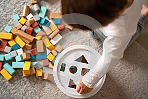 Top view of little toddler boy playing with wooden colorful building blocks sorting shapes