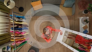 Top view of living room. Girl in beautiful dress standing near the mirror, holding smartphone and taking selfie pictures