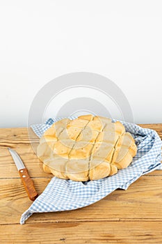 Top view of loaf of rustic bread on cloth and wooden table with knife, white background, vertical,