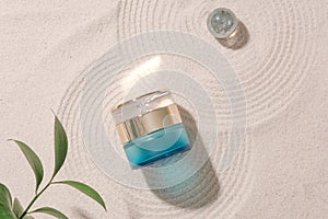 Top view of a luxurious lotion jar placed on a smooth sand background with a glass marble, with green leaves in the corner of the