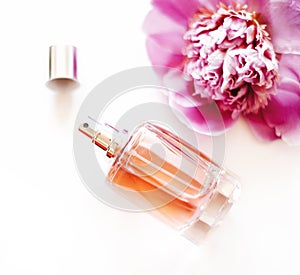Top view of luxury perfume bottle and pink peony flower on white background. Female cosmetic and makeup accessory still life