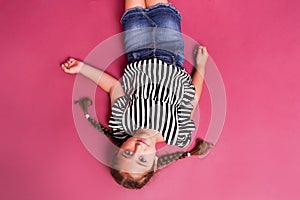 Top view of lying ittle happy girl on a pink background