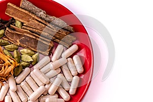 Top view macro shot of cinnamon sticks, cardamom, clove and nutmeg aril with herbal capsules in a red plate on copy space white photo