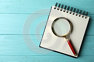 Top view of magnifier glass and empty notebook on blue wooden background, space for text. Find keywords concept