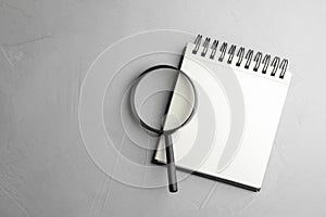 Top view of magnifier glass and empty notebook on grey stone background, space for text. Find keywords concept