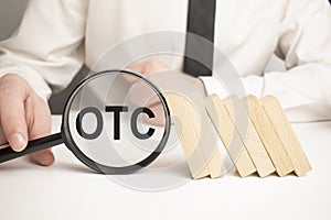 Top view of magnifying glass and alphabet letters with text OTC stands for Over-the-counter. Business concept