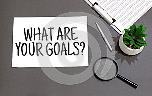 Top view of magnifying glass,calculator,pen, plant and notebook written with WHAT ARE YOUR GOALS sign