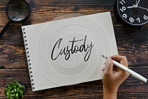 Top view of magnifying glass,clock,plant and hand holding pen writing custody on notebook