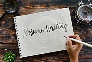 Top view of magnifying glass,clock,plant,pen with hand writing & x27; Resume Writing & x27; on a notebook on wooden background