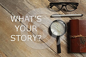 Top view of magnifying glass,notebook,pen, and glasses on wooden background written with question What& x27;s Your Story.