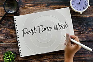 Top view of magnifying glass,plant,clock and hand holding pen writing Part Time Work on notebook on wooden background