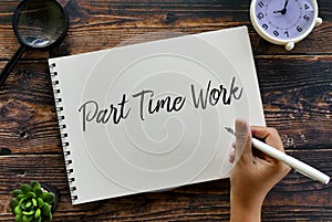 Top view of magnifying glass,plant,clock and hand holding pen writing Part Time Work on notebook on wooden background photo