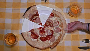 Top view of male, female and newborn baby hands taking slices of pizza with tomato, cheese and salami.