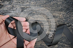 Top view of male hand holding black ribbon on dark wood background with copy space. Melanoma or skin cancer, gang prevention