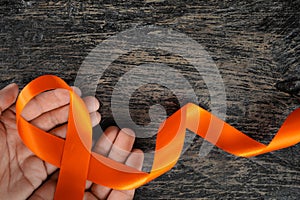 Top view of male hand holding orange ribbon on dark wood background. Leukemia, kidney cancer, adhd, copd, malnutrition and hunger.