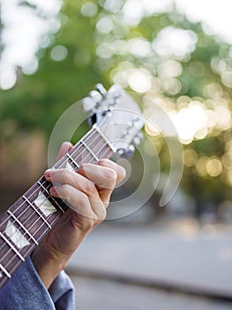 A top view on male hand plays guitar in a jeans jacket in a park on a blurred background. photo
