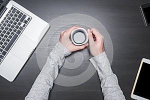Top view of Male hands holding a coffee cup with laptop, tablet and smart phone on black wooden table background.