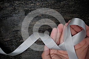 Top view of male hands holding gray ribbon on dark wood background with copy space. Brain cancer tumor awareness concept. photo