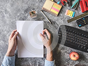 Top view of Male hands holding paper sheet with Office supplies on Grunge gray background.