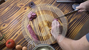 Top view male hands with knife cutting on slices pepperoni sausage on wooden table. Chef cook cutting sausage salami on