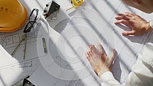 Top view male hands laying out blueprints on the white table lit by the sun