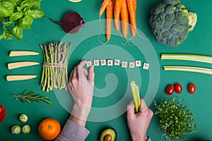 Top view male hands laying out word Veganuary on the green background with set of fresh raw vegetables and fruits. Vegetarian and