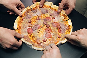 Top view male hands taking slices of pizza with cheese, tomatoes and ham from food delivery. Group of hungry friends