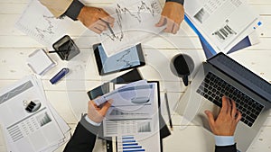 Top view male hands of two businessmen looking and examining graphs with financial reports in office. Business partners