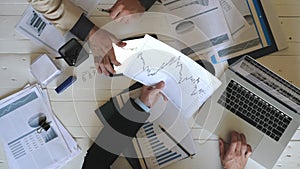 Top view male hands of two businessmen looking and examining graphs with financial reports in office. Business partners