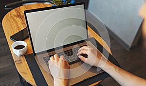 Top view of male hands typing on computer keyboard; man working on laptop; smartphone and coffee cup on wooden table.