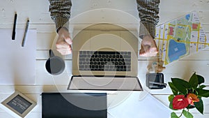Top view on male hands typing text on laptop keyboard at white wooden desk. Creative businessman celebrating achievement